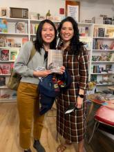 Two women standing next to each other, one holds a book