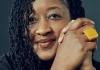 A headshot photo of LaShawnDa smiling with her hands clasped together in front of a dark gray background