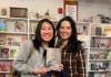 Two women standing next to each other, one holds a book