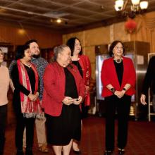 Seven individuals stand together to the right of the podium looking on as the main speaker for American Ethnic Studies talks with the audience