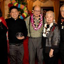 Five individuals stand next to each other facing the camera as one holds the Golden Circle Award in his left hand