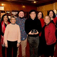 Nine individuals standing together, smiling, the center person, Rick Bonus, Chair of the AES Department, holds the Golden Circle Award given to AES